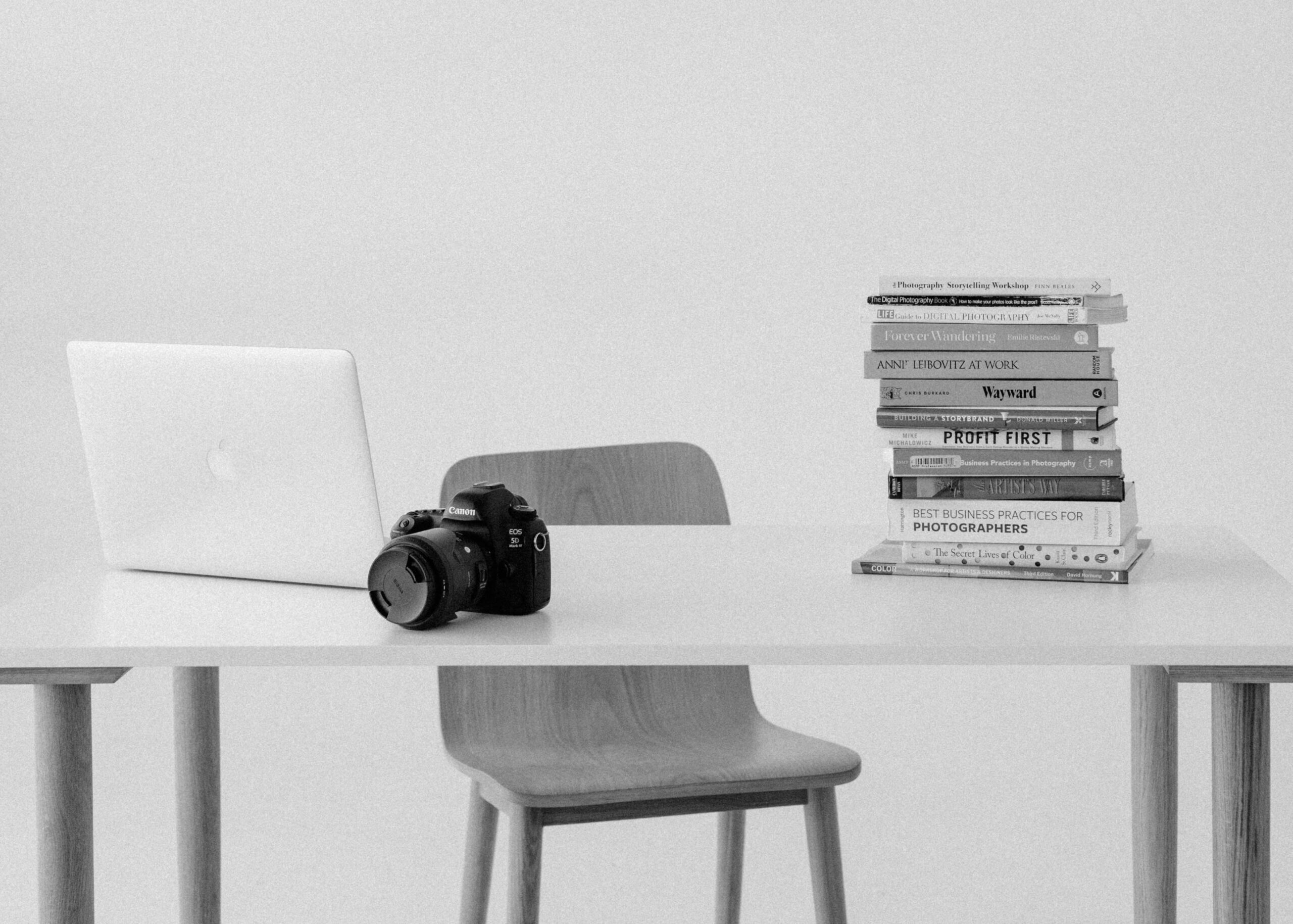A laptop, camera, and books are styled on top of a desk.